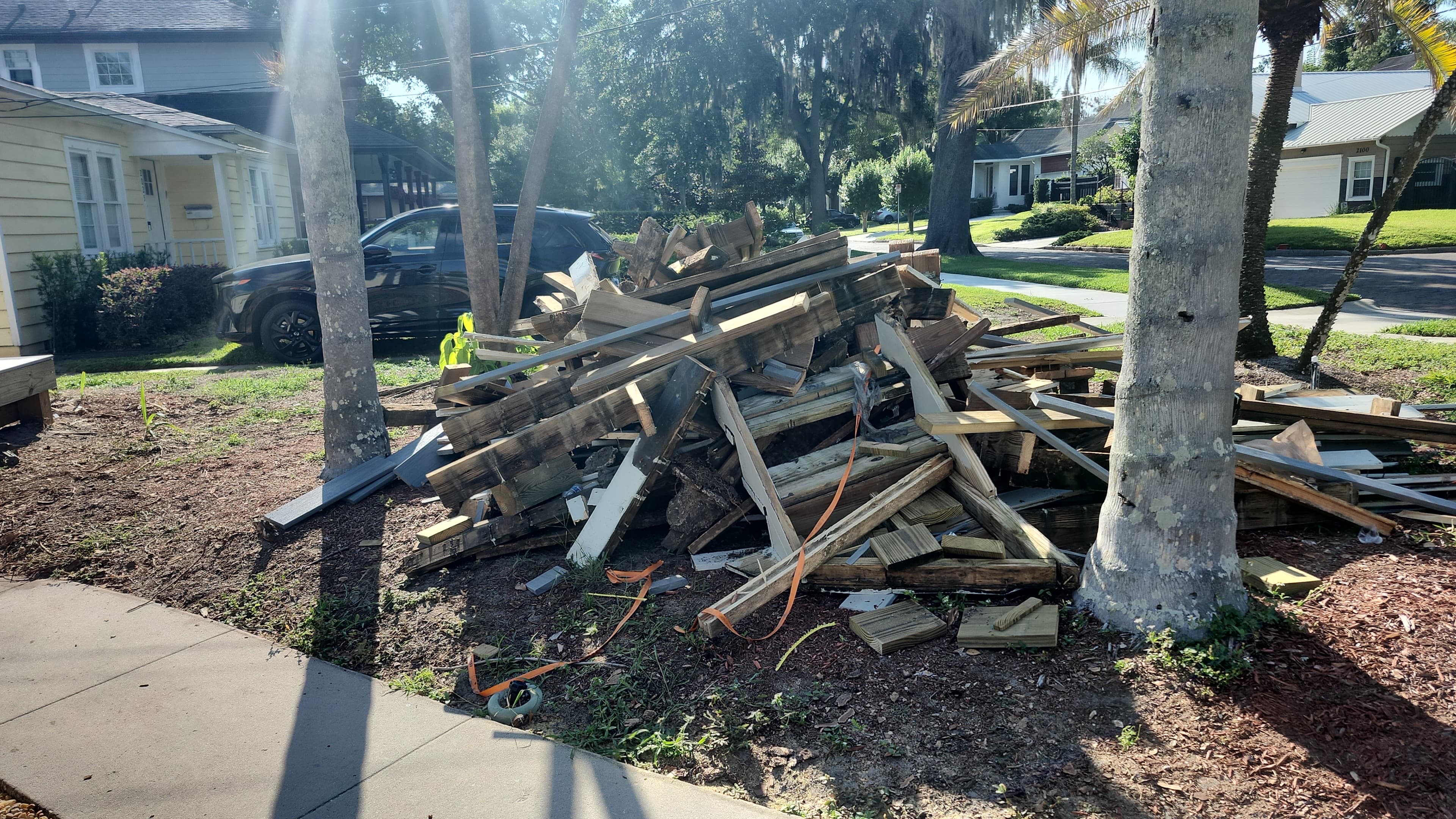 Before: Demolished deck lumber piled between palm trees in Orlando front yard