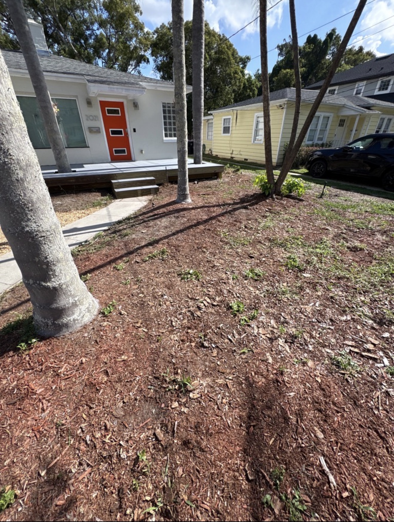 After: Clean yard with house and orange front door visible — deck demolition debris completely removed